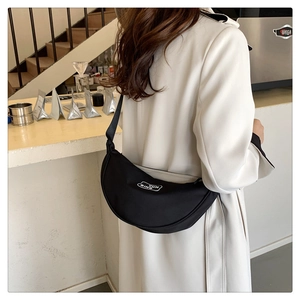 Outdoor shot of minimalist black crescent crossbody bag with white brand logo patch