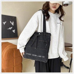 Detailed view of black denim tote bag featuring utility pockets and street embroidery