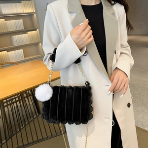 Detail of black faux fur shoulder bag with white pompom charm and gold chain strap