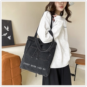 Close-up of black denim tote bag featuring dual front pockets and white embroidered text