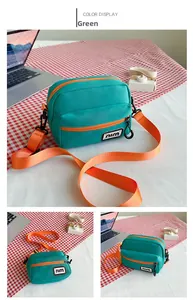 Detail view of green canvas crossbody bag featuring contrasting orange zipper and strap
