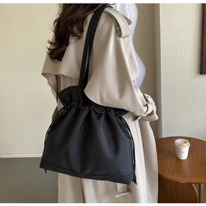 Side view of a woman wearing a black drawstring nylon tote bag with elegant folds