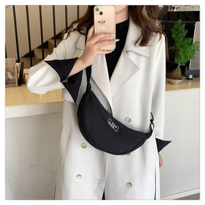 Detail of black crescent crossbody bag with white brand label and adjustable strap
