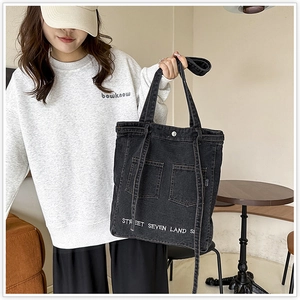 Detail of black denim tote bag with cargo pockets and white text print decoration