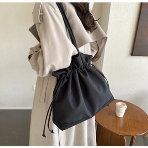 Detail shot of black drawstring bucket shoulder bag carried by a model in a beige coat