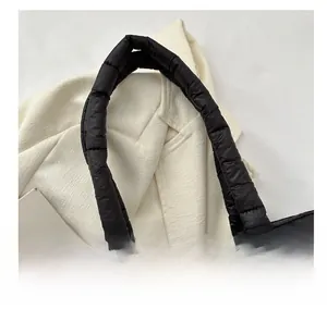 Close-up of padded quilted handles on a black down tote bag with high-gloss finish