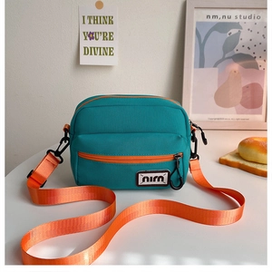 Detail view of the green canvas crossbody bag featuring a vibrant orange zipper and strap