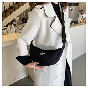 Detail of black crescent crossbody bag showing white logo print and adjustable nylon strap