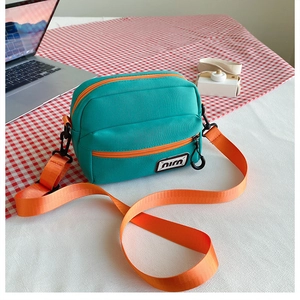Detail of teal nylon crossbody bag with bright orange straps and dual zipper pockets