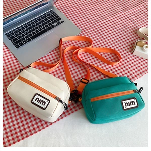Detail of canvas crossbody bags in cream and green with orange nylon shoulder straps
