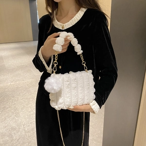 Detail of white plush handbag featuring faux fur pom-pom handle and gold metal chain