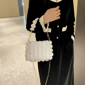 Detail of white plush shoulder bag with wavy edges, gold chain, and faux fur pompom handle