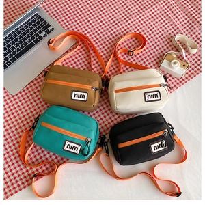 Flat lay of four colorful canvas crossbody bags with bright orange straps on plaid cloth