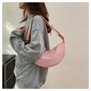 Pink crescent shoulder bag side view showing adjustable strap and brand tag on female model