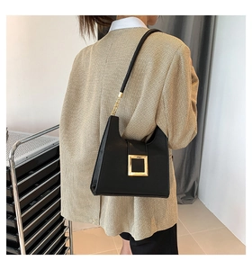 Side view of a black leather crossbody bag with a gold square buckle on a plaid blazer