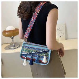 Detail of bohemian ethnic embroidered bag with colorful tassels and wide woven strap