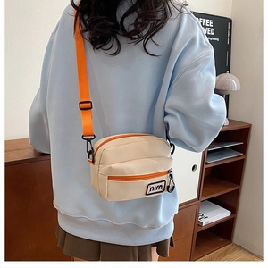Detail of minimalist canvas crossbody bag with orange strap and front zipper pocket