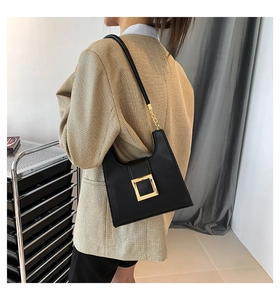 Detail view of a black leather crossbody bag featuring a large square golden buckle on the strap