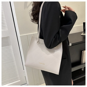 Détail d'un sac fourre-tout matelassé beige porté par un mannequin en costume noir chic