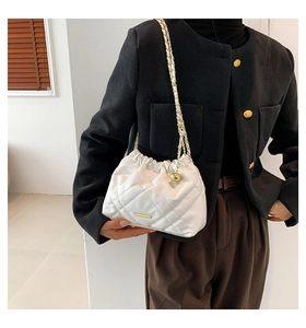 Detail of white quilted bucket bag with gold chain strap and metallic ball charm