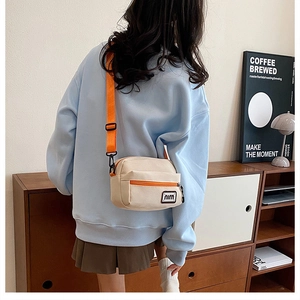 Detail of minimalist beige canvas crossbody bag with bright orange strap and mini logo tag