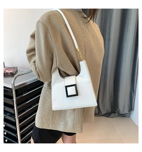 Detail of white cross-body bag featuring a black buckle and gold chain strap
