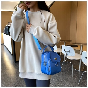 Compact blue nylon crossbody bag shown on a model in a stylish cafe setting