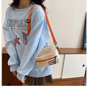 Detail of cream canvas crossbody bag with orange zipper and adjustable woven shoulder strap