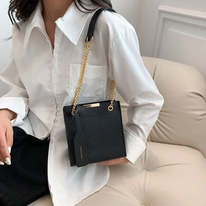 Detail of black geometric quilted crossbody bag with gold chain strap and fashion tag