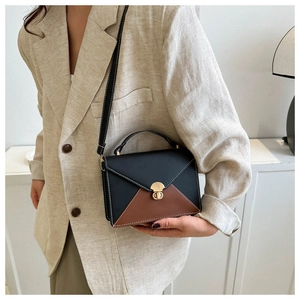 Détail du sac enveloppe bicolore avec fermoir doré sur une tenue en lin chic