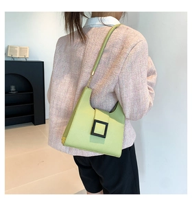 Green leather crossbody bag with black buckle worn by a model in a modern room