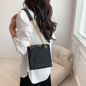 Fashionable black quilted crossbody bag with gold chain strap in a modern minimalist setting