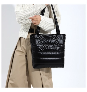 Detail of black quilted puffer tote bag in glossy nylon fabric on fashion model