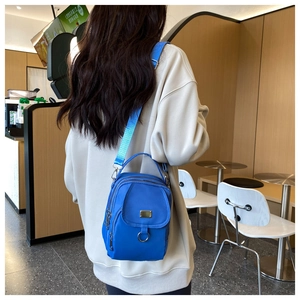 Blue nylon mini crossbody bag with multiple zippers and adjustable straps worn by a model