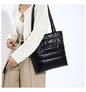 Detail of black quilted puffer tote bag with glossy finish and soft padded shoulder strap