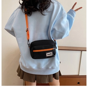Detail view of the black canvas crossbody bag with orange accents on a model's back
