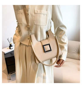 Detail view of beige square crossbody bag with black buckle and gold chain strap