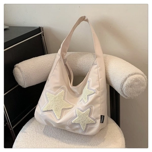 Detail of cream canvas tote bag featuring yellow star embroidery and fashion tag