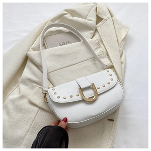 Détail du sac selle blanc avec rivets dorés et boucle en U sur un blazer beige