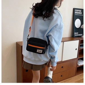 Detail showing contrast orange zipper and strap on minimalist black canvas crossbody bag