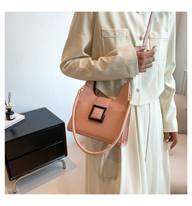 Pink crossbody bag with black square buckle shown on model in minimalist setting