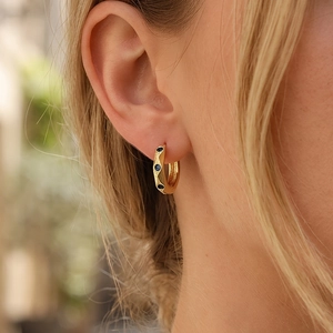 Detailed view of a gold hoop earring set with blue stones on a model's ear
