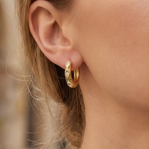Detail of gold hoop earring with rhombus texture and three sparkling zircons on ear