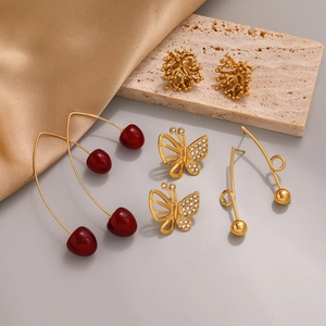 Macro shot of assorted gold earrings featuring red cherries and hollow butterfly designs