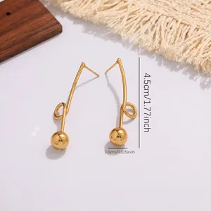 Detail view of geometric drop earrings featuring a long curved bar and golden ball charm