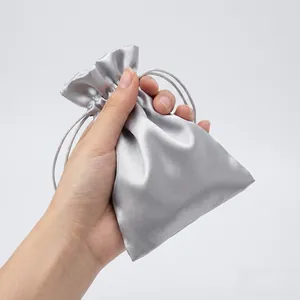 Hand holding silver satin drawstring bag with silky texture and metallic sheen finish