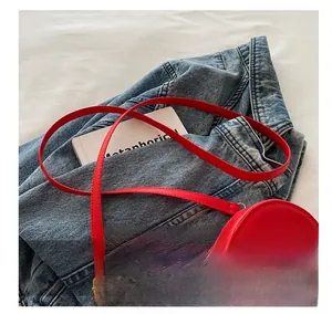Detail of red heart-shaped PU leather crossbody bag on blue denim jacket background