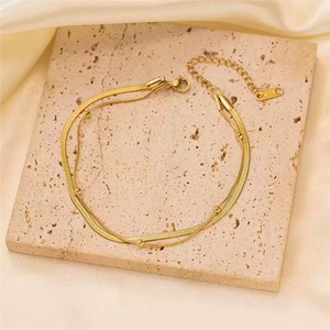 Elegant gold-tone layered necklace with flat snake chain and beaded strand on stone tray