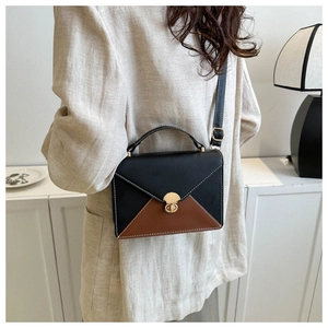 Détail du sac enveloppe bicolore avec fermoir rotatif doré sur un blazer beige chic