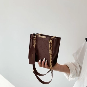 Detailed macro of chocolate brown quilted crossbody bag with gold chain and metal bar handle